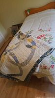 Quilt and comforter displayed on a bed, showing folded quilt on comforter with visible floral pattern.