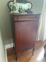 Front view of the vintage wooden music cabinet showing drawer, cabinet door with carved decoration, and mirrored back.