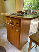 Front-left angle showing the center drawer with white ceramic knob and two-door lower cabinet with matching knobs. Some kitchen items placed on top but not included.