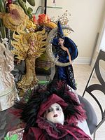 Full view of both Barbie dolls displayed on a glass table with a flower bouquet background and one other porcelain figure visible.