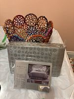 Two queen pillow cases and a blanket in original plastic packaging with gray floral pattern, with colorful fabric basket behind