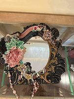 Top view of ornate ceramic and glass mirror frame featuring pink rose, grapes, leaves in ceramic relief with painted gold embellishments.