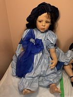 Front view of fabric doll wearing blue dress and matching blue velvet ribbon hat, showing facial details and full outfit.