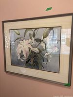 Full view of framed flower print artwork hanging on wall, showing white lilies and green leaves on a bluish background.