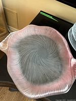 Large pink-tinted glass platter with spiral pattern and handles on both sides, displayed on a dark surface.