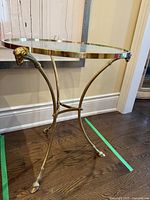 Full view of small round glass table with gold colored metal frame and sculptural lamb head accents on legs.