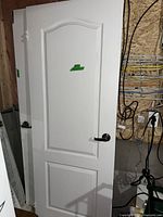 White interior door with two raised rectangular panels and brushed silver lever handle, positioned upright with a wall and wiring in background.