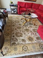 Full view of rectangular wool rug spread in living area with floral pattern, beige and gold tones, fringed edges.