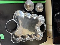 Front view of the metal serving dish with two removable small metal cups separated from the tray, showing the scalloped edge design and handles.