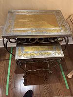 Two metal nesting side tables stacked together, showing rectangular top surfaces with gold and silver decorative finish and scroll metal legs.