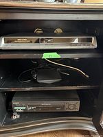 Front view of Panasonic DVD Recorder DMR-EH55 showing DVD and SD card slot, and Sony VCR player below on shelf.