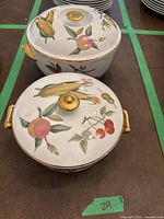 Two Royal Worcester porcelain casserole dishes with lids, decorated with fruit motifs and gold accents on a table
