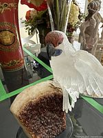 Front view of clear quartz parrot perched on brown geode slice with stand