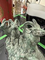 Front and side view of metal ram sculpture showing four rams on textured base with wooden framing