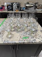 14 clear glass wine stemware pieces displayed on a counter, including larger and smaller glasses with olive green ribbed stems.