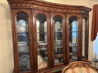 Front view of wood and glass china cabinet showing glass doors with shelves inside containing various dishware.