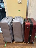 Side view showing two gray softside luggage pieces and one red hard shell suitcase.