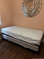 Twin trundle bed showing main bed with mattress and the trundle bed pulled out beneath it also with mattress, framed with metal.