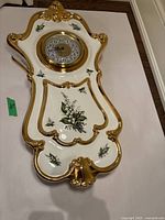 Full view of the Italian white ceramic wall clock with gold accents and floral designs, showing overall shape and clock face