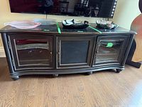 Full frontal view of the wooden TV stand showing three front panels, two with glass doors and a fabric-covered center panel, with some items placed on top.
