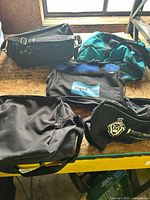 Four black bags displayed on a wooden surface under natural light, showing variety in style and logos.