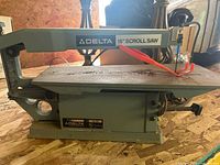 Side profile showing scroll saw body with motor and 15-inch worktable marked "15" SCROLL SAW" label and "DELTA" brand name.