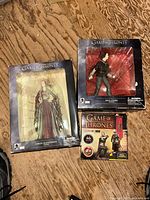 Photo showing all three boxed Game of Thrones collectible figures of Arya Stark, Cersei Baratheon, and Jaime Lannister on a wooden floor.