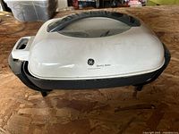 White GE electric skillet with black base and glass window lid placed on wooden surface.