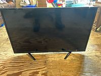 Front view of the flat screen TV on a wooden floor showing its stand and screen size
