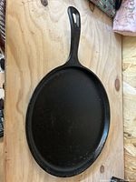 Round cast iron griddle with integrated handle on wood surface