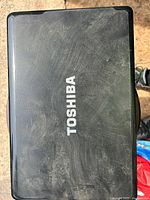 Closed black Toshiba laptop lid with visible scratches and dust showing brand logo.