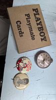 Set showing Playboy Playmate Cards box, two collectible pins (Santa and Joe DiMaggio), and Westclox pocket watch on white surface.