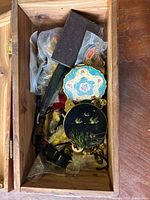 Wooden box containing assorted vintage items including decorative compacts, small boxes, and plastic bags with pins and button covers