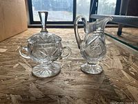 Crystal sugar bowl with lid and matching creamer on wood surface, showing overall design and shape.