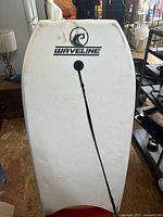 White top side of the Waveline bodyboard showing logo and attached black leash, minor wear visible.
