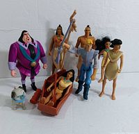 Eight Pocahontas-themed action figures and one finger puppet arranged with Pocahontas in a brown canoe boat, characters John Smith, Chief Powhatan, Nakoma, John Ratcliffe, Percy bulldog, and an additional finger puppet figure.