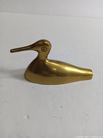 Side view of the vintage brass duck mallard paperweight showing the smooth polished gold brass surface and the simple stylized shape.