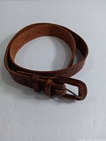 Rolled brown leather belt showing surface texture and buckle area.
