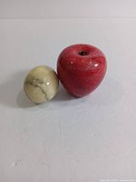 Red marble apple and cream-colored marble egg side by side on a white surface.
