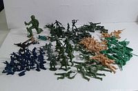 Overview photo showing a mix of green, brown, khaki Tim Mee plastic army men and smaller blue soldiers arranged on a white background.