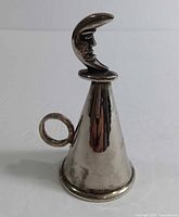 Front view of vintage silver tone metal candle snuffer showing crescent moon top and ring holder.