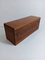 Front angled view of vintage wood recipe box showing carved 'RECIPES' wording and decorative carving details.