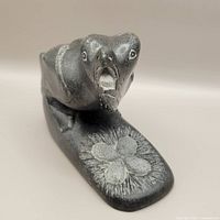 Front perspective of dark stone carving showing bird with open beak and nest with eggs on base.