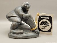Side view of gray stone carving showing the hunter crouched with the seal. Eskimo Art tag attached.