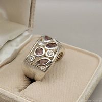 Close-up front angle of sterling silver ring featuring pink teardrop and oval stones with clear round stones, displaying intricate setting details.