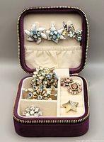 Full view of the vintage costume jewelry lot inside plum velvet La Kaiser travel case showing earrings, brooches, and ring with iridescent rhinestones.