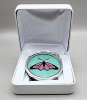 Pendant with butterfly design encased in glass set in sterling silver shown resting inside white jewelry box.