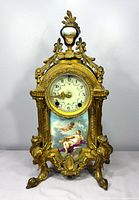 Front view showing the clock's ornate brass frame, clock face with floral dial, and porcelain panel with classical painted figures.