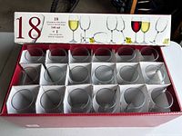 Box containing 18 empty wine glasses arranged in individual slots inside a red storage box with white dividers. The box lid shows illustrations of wine glasses with liquids.