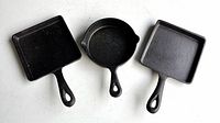 Three small cast iron pans placed side by side on a flat surface, showing front view of pans and handles.